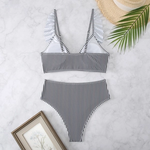 Flat lay of striped bikini with ruffle straps and high waist bottom on marble background