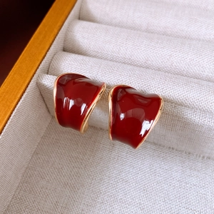 Close-up of red enamel C-shape wide earrings with gold plating on beige fabric
