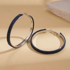 Detailed close-up of large blue denim wrapped hoop earrings with silver metal inner band