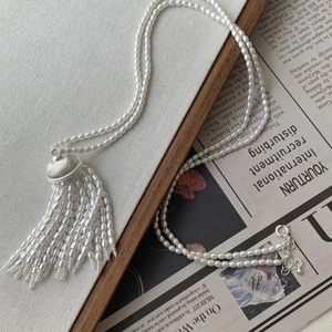 Detail of white pearl strand necklace featuring a metallic wheat tassel pendant charm