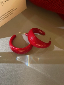 Gros plan sur des boucles d'oreilles en acrylique rouge en forme de C avec tiges argentées