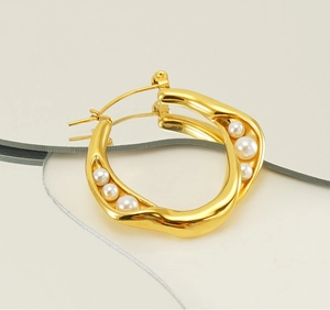 Detail view of wave-shaped golden hoop earring with inlaid white pearls on reflective surface