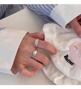 Detail showing s925 silver bow and heart rings worn on a hand against white fabric