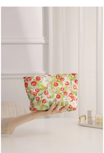 Primer plano de un neceser con estampado floral de bayas rojas sostenido por la mano.