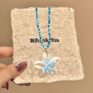 Detail of blue beaded necklace with white shell flower pendant for a coastal beach look