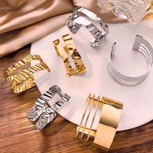Elegant gold and silver irregular wavy cuff bracelets displayed on silk and ceramic tray