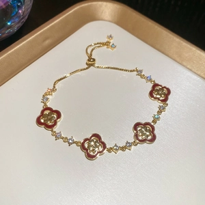 Détail du bracelet trèfle réglable avec chaîne dorée et pierres rouges