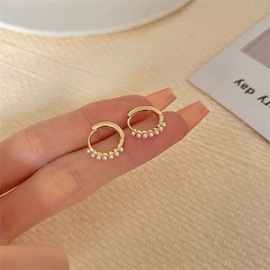 Minimalist gold hoop earrings with small pearls held by hand for scale and detail