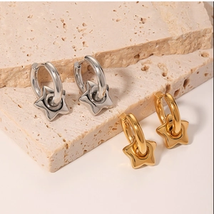 Close-up of geometric star charm hoop earrings in gold and silver finish on beige stone
