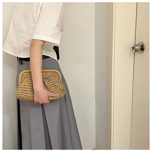 Detailed close-up of a beige straw clutch bag held by a model against a white wall