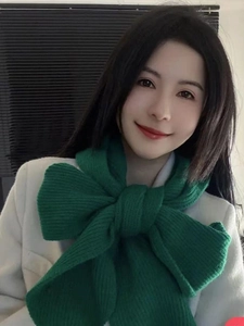 Detail of green knitted scarf tied in a large bow showcasing thick and soft texture