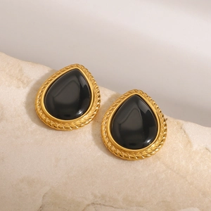 Gros plan de boucles d'oreilles goutte dorées avec gemme noire ovale sur pierre beige