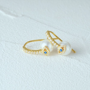 Macro shot of S925 silver gold pearl earrings featuring blue evil eye charms