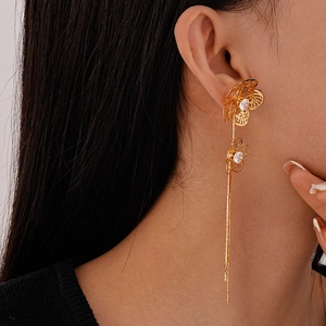 Detail of long gold tassel earrings with hollow flowers and sparkling crystals on model