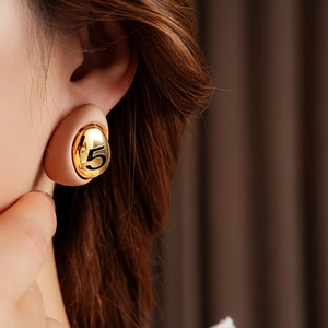 Close-up of a gold-plated teardrop earring with beige enamel and number 5 on a model