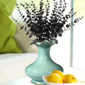 Detail of artificial black eucalyptus stems in a light blue wavy ceramic vase
