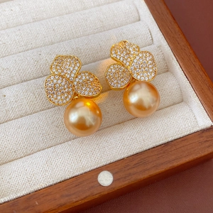 Macro shot of gold-plated flower earrings with zircon petals and pearls on velvet