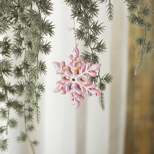 Pink resin snowflake donut ornament with colorful sprinkles hanging on a Christmas tree