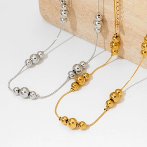 Collier à billes en acier inoxydable poli doré et argenté sur un support en pierre