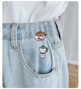 Detail of coffee cup and moka pot enamel pins on blue denim fabric pocket edge