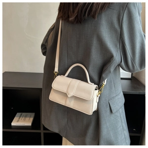Detail view of cream crossbody bag with vertical stitching and gold hardware on grey blazer