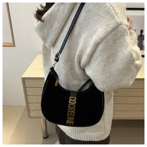 Detail of black crescent shoulder bag with gold metal logo worn by a model in a minimalist setting