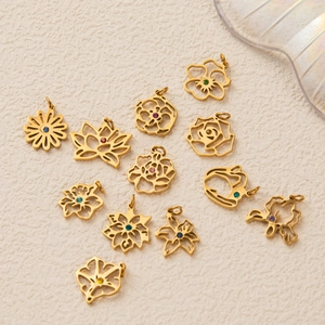 Set de 12 pendentifs fleurs en acier titane avec zircons colorés sur fond beige texturé