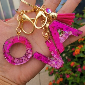 Pink glitter resin letter keychain detail shot, epoxy alphabet charm with gold clasp and tassel.