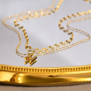 Close-up of double layer gold necklace with crystal H letter pendant on mirror