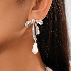Gros plan de boucles d'oreilles nœud argentées avec cristaux et pendentif perle blanche