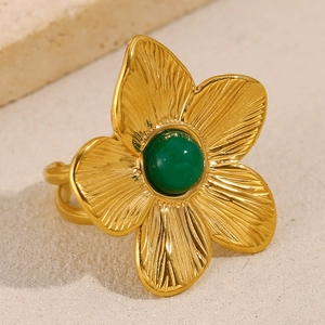 Detail of 18K gold flower ring with green stone and brushed metal texture