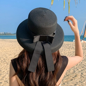 Detail of a black straw beach hat with a matching bow ribbon in a sunny seaside setting