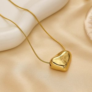 Macro shot of gold heart pendant on snake chain over beige silk and white ceramic