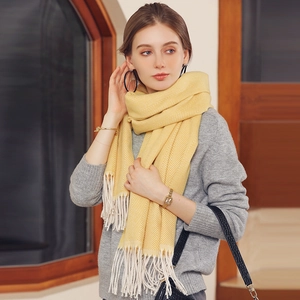 Elegant yellow herringbone knit scarf with fringe tassels worn by a model in a cozy room