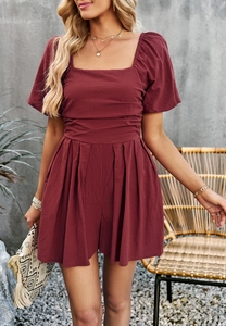Detail of wine red square neck romper with puff sleeves and cinched waist on a terrace