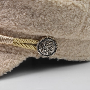 Macro detail of beige textured fabric newsboy cap with gold braided rope and vintage button
