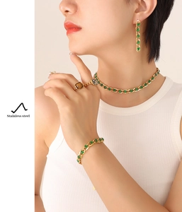 Close-up of gold stainless steel jewelry set featuring green crystals on a female model