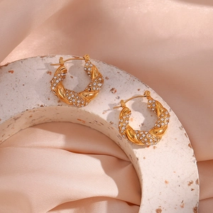 Detail of gold twisted hoop earrings with cubic zirconia on silk background