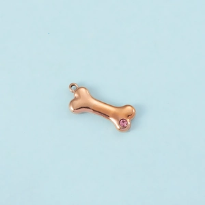 Detail of rose gold bone pendant with pink zircon inlay on a clean blue background