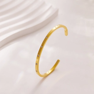 Detail view of a 18k gold-plated C-shaped steel cuff bracelet with five inlaid zircons