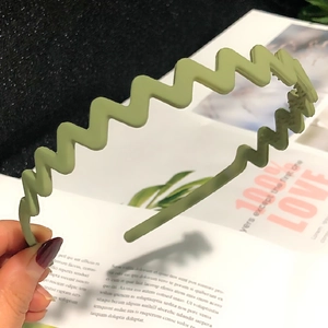 Close-up of a green wavy candy-colored plastic headband held by hand with natural lighting