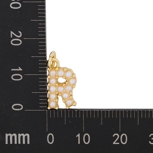 Macro shot of gold letter R pendant with pearls next to a ruler for size measurement