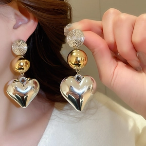 Macro detail of oversized mixed-metal heart earrings with glossy silver and gold finish
