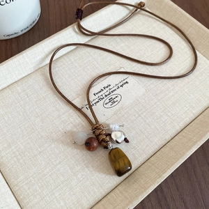 Macro detail of wax rope necklace with tiger eye stone and wooden beads on beige tray