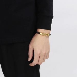 Detail of black braided leather bracelet with golden infinity symbol on a male wrist
