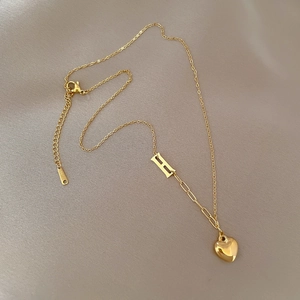Detailed view of gold titanium steel necklace featuring H pendant and heart charm