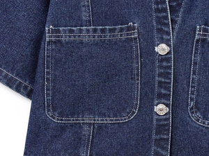 Détail d'une veste en jean bleu foncé avec coutures blanches et boutons métalliques