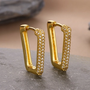 Macro view of gold geometric hoop earrings with pavé cubic zirconia on stone background