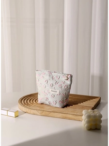 Embossed floral makeup bag with pearl zipper on a stylish wooden tray display