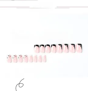Detailed view of pink press-on nails with black French tips and white star accents